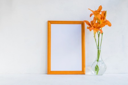 Mockup with a golden frame and orange summer flowers in a vase on a light backgroundの写真素材