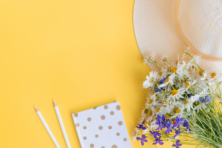 Flat lay desk with summer hat, flowers and notebook on yellow backgroundの写真素材