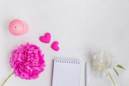 Flat lay desk with pink peony, notebook and accessories on light backgroundの写真素材