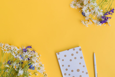 Flat lay desk with summer flowers and notebook on yellow backgroundの写真素材