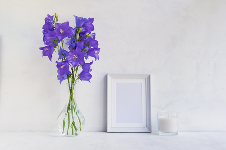 Mockup with a white frame and summer blue flowers in a vase on a light backgroundの写真素材