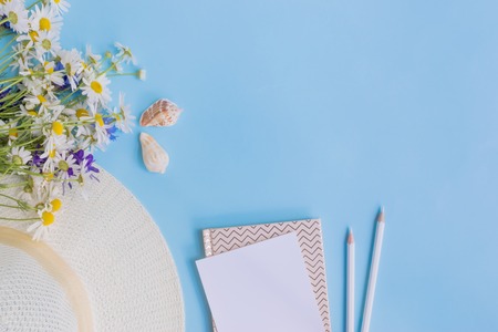 Flat lay desk with summer hat, flowers and notebook on blue backgroundの写真素材