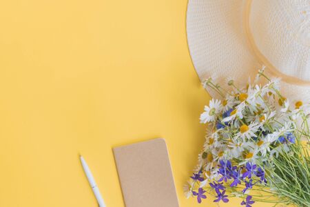 Flat lay desk with summer hat, flowers and notebook on yellow backgroundの写真素材