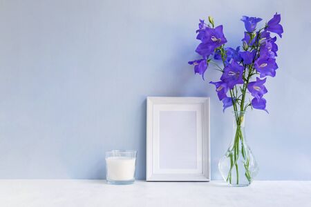 Mockup with a white frame and summer blue flowers in a vase on a light blue backgroundの写真素材