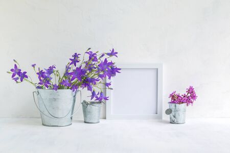 Mockup with a white frame and summer flowers in a metal bucket on a light backgroundの写真素材