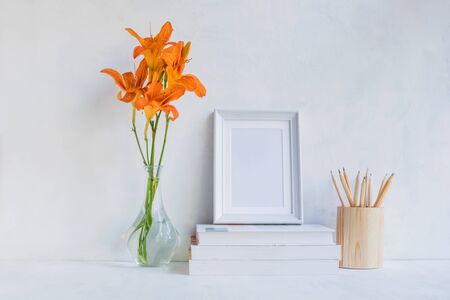 Home interior with decor elements. White frame, flowers in a vase, books and pencilsの写真素材
