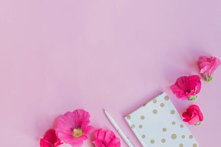 Flat lay desk with pink flowers and notebook on pink backgroundの写真素材
