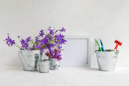 Mockup with a white frame and summer flowers in a metal bucket and garden tools on a light backgroundの写真素材