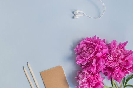 Flat lay desk with pink peonies, notebook and accessories on light blue backgroundの写真素材