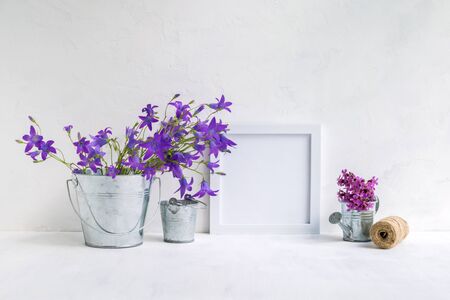 Mockup with a white frame and summer flowers in a metal bucket on a light backgroundの写真素材