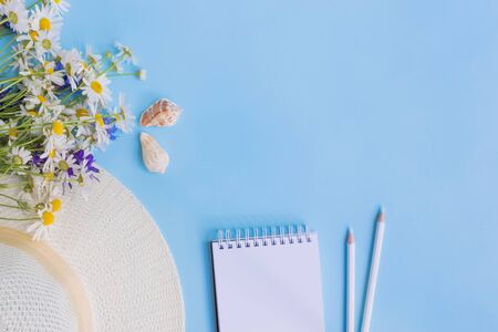 Flat lay desk with summer hat, flowers and notebook on blue backgroundの写真素材