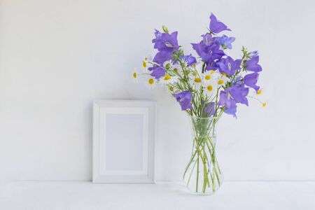 Mockup with a white frame and summer blue flowers in a vase on a light blue backgroundの写真素材