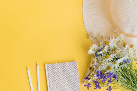 Flat lay desk with summer hat, flowers and notebook on yellow backgroundの写真素材