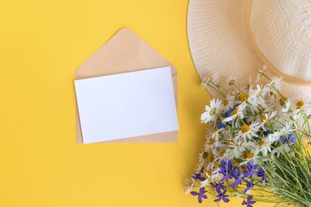 Mockup white greeting card and envelope with summer hat and flowers on a yellow backgroundの写真素材