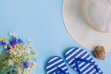 Summer hat, flowers and flip flops on a blue background. Top view, flat layの写真素材