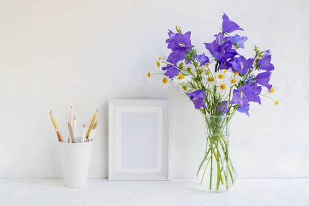 Mockup with a white frame and summer blue flowers in a vase on a light backgroundの写真素材