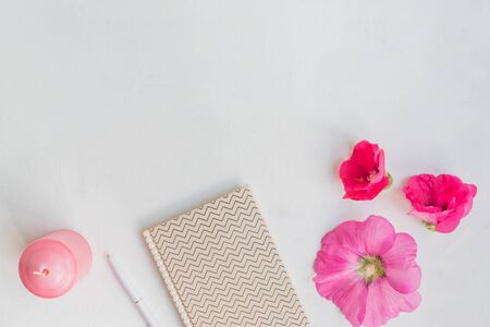 Flat lay desk with pink flowers, notebook and accessories on light backgroundの写真素材