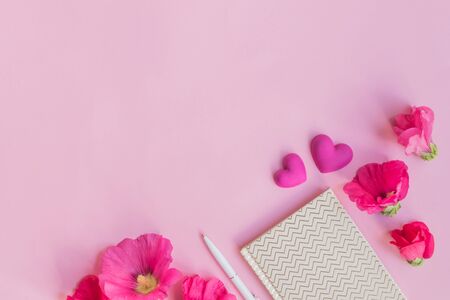 Flat lay desk with pink flowers and notebook on pink backgroundの写真素材