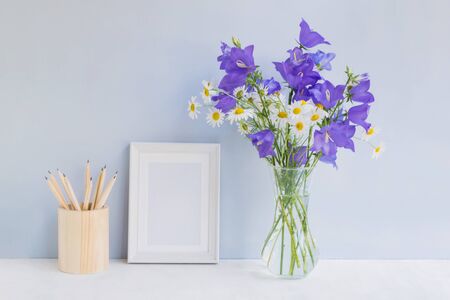 Mockup with a white frame and summer blue flowers in a vase on a light blue backgroundの写真素材