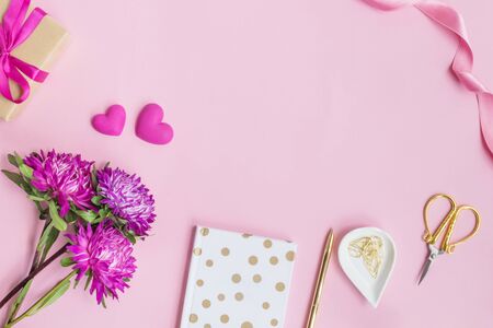 Flat lay desk with pink flowers, notebook and red hearts on a pink backgroundの写真素材