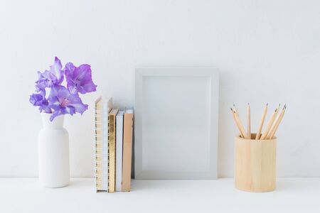 Home interior with decor elements. White frame, flowers in a vase, books and pencilsの写真素材
