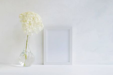 Mockup with a white frame and white flower hydrangea in a vase on a light backgroundの写真素材