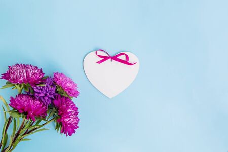Bouquet with pink flowers and white heart on blue background empty space for your text, top viewの写真素材