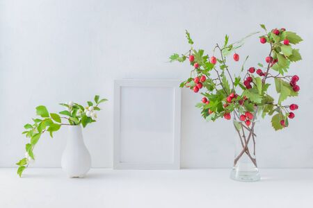 Mockup white frame and branches with red berries in a vase on a light backgroundの写真素材