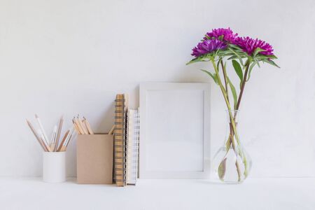 Home interior with decor elements. White frame, flowers in a vase, books and pencilsの写真素材