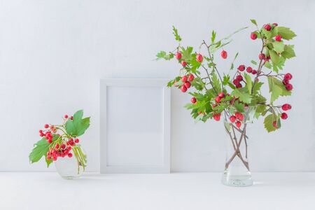 Mockup white frame and branches with red berries in a vase on a light backgroundの写真素材