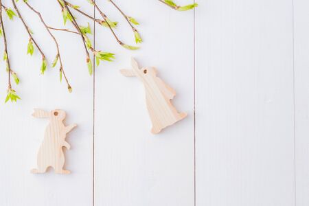 Flat lay easter composition with green buds on branches and rabbit on a white wooden background