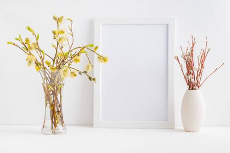 Home interior with easter decor. Mockup with a white frame and willow branches in a vase on a light backgroundの写真素材