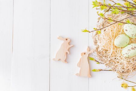 Flat lay easter composition with green buds on branches and eggs on a white wooden background