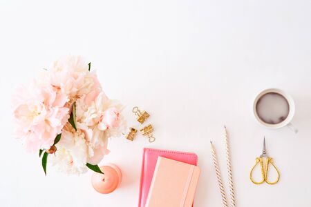 Flat lay blogger or freelancer workspace with a notebook and pink peonies on a white backgroundの写真素材