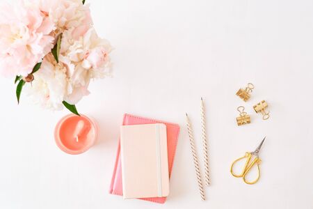 Flat lay blogger or freelancer workspace with a notebook and pink peonies on a white backgroundの写真素材
