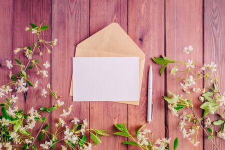 Mockup white greeting card and envelope with spring white flowers on a wooden background