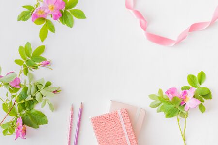 Flat lay blogger or freelancer workspace with a notebook, pink flower on a white backgroundの写真素材