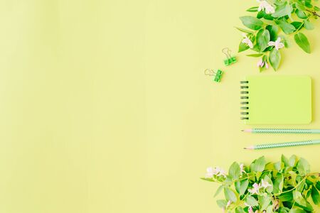 Flat lay blogger or freelancer workspace with a notebook, branches and green leaves on a green backgroundの写真素材