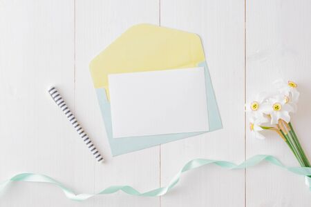 Mockup white greeting card and envelope with white daffodils on a white wooden table