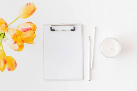 Flat lay blogger or freelancer workspace with a mockup clipboard and yellow tulips on a light...