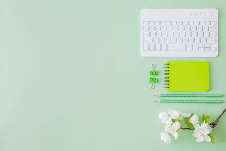 Flat lay blogger or freelancer workspace with a notebook, keyboard and white spring flowers on a green backgroundの写真素材