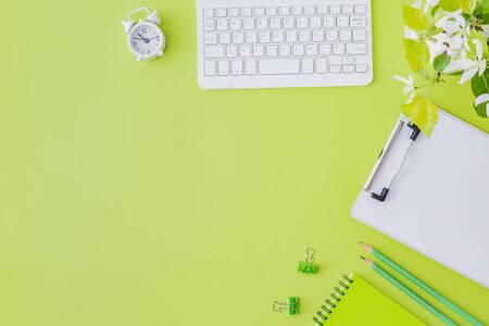 Flat lay blogger or freelancer workspace with a notebook, keyboard and white spring flowers on a green backgroundの写真素材