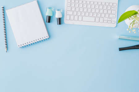 Flat lay blogger or freelancer workspace with a notebook, keyboard and lily of the valley flowers on a blue backgroundの写真素材