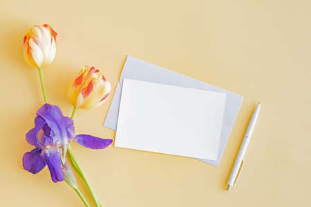 Mockup white greeting card and envelope with yellow tulips and blue irises on a yellow backgroundの写真素材