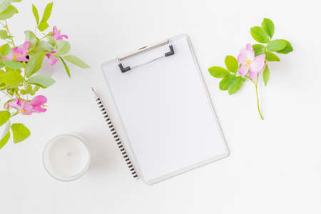 Flat lay blogger or freelancer workspace with a clipboard, pink flowers on a white background
