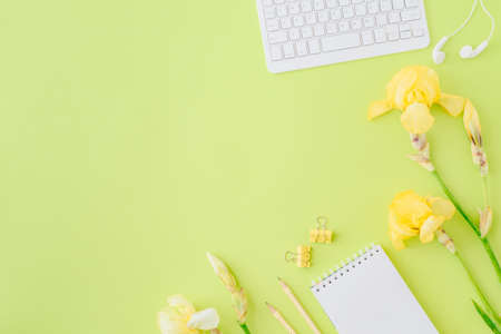 Flat lay blogger or freelancer workspace with a notebook, keyboard, yellow irises on a green backgroundの写真素材