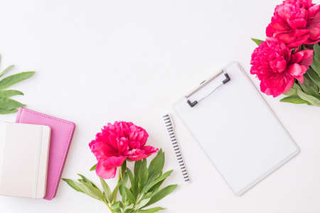 Flat lay blogger or freelancer workspace with a notebook, clipboard, red peonies on a white backgroundの写真素材
