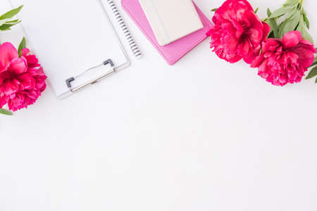 Flat lay blogger or freelancer workspace with a notebook, clipboard, red peonies on a white...