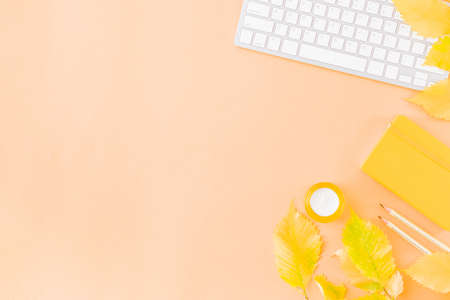 Flat lay blogger or freelancer workspace with a notebook, keyboard, colorful autumn leaves on a color backgroundの写真素材