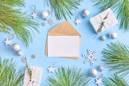 Mockup white greeting card and envelope with pine branches and gift box on a blue backgroundの写真素材